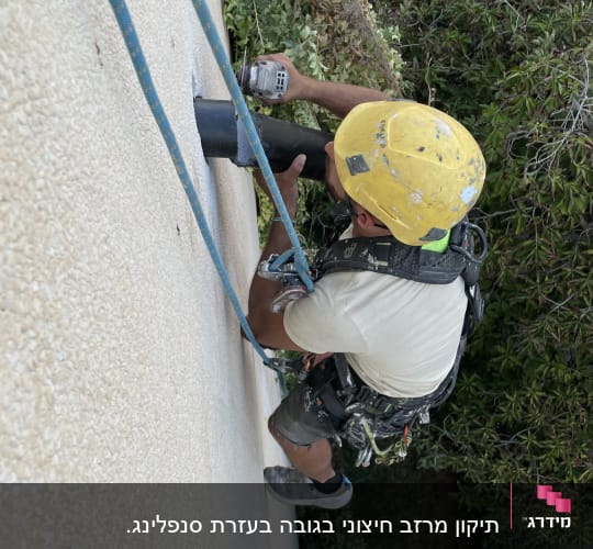 עובד בגובה עם קסדה צהובה ומקדחה
